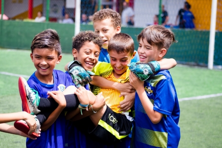 Grupo de alunos mirins sorrindo e se abraçando em comemoração no campo de grama sintética